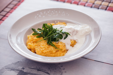 Fresh made cooked polenta served with cream cheese sauce and rocket leaves - rucola in plate at dining table