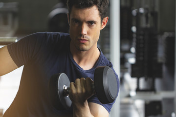 Fototapeta na wymiar Young Man lifting dumbbells in gym, healthy lifestyle concept, With many gym equipment as background.