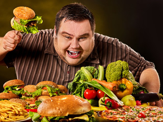 Diet fat man who makes choice between healthy and unhealthy food. Overweight male with hamburgers,...