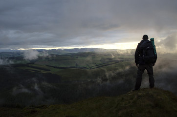 Hiker Looking Over Green Hills at Sunset