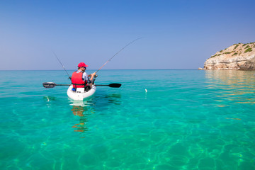 Man fishing on a kayak in the sea with clear turquoise water. Fisherman kayaking in the islands. Leisure activities on the ocean.