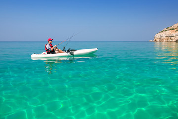 Man fishing on a kayak in the sea with clear turquoise water. Fisherman kayaking in the islands. Leisure activities on the ocean.