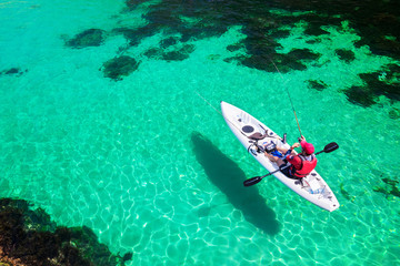 Man fishing on a kayak in the sea with clear turquoise water. Fisherman kayaking in the islands....