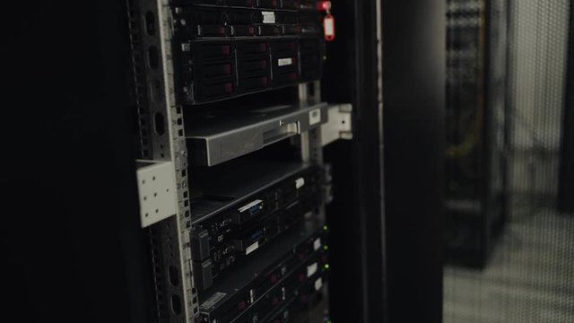  IT engineer is working in a data center with rows of server racks and super computers. He check cables and other equipment.