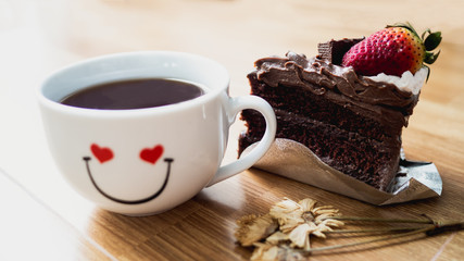 Black coffee In white glass with soft chocolate cake and dried flowers on the wood floor.
