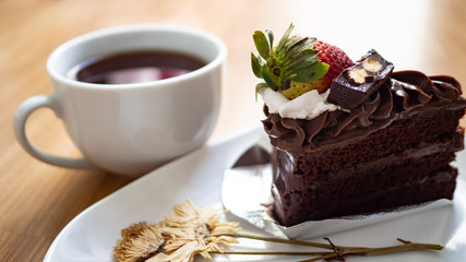 Black coffee In white glass with soft chocolate cake and dried flowers on the wood floor.