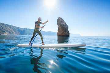 Stand up paddle boarding. Young man floating on a SUP board. The adventure of the sea with blue water on a surfing - obrazy, fototapety, plakaty