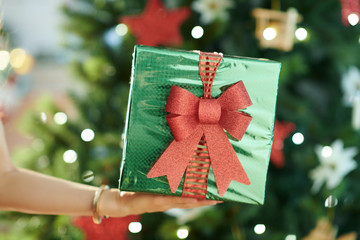 green Christmas present box in hand of woman near Christmas tree