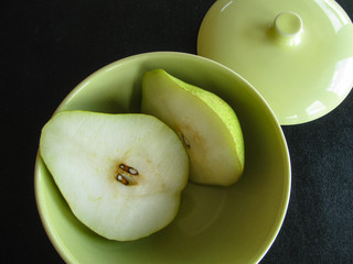 Still life with fresh cut pear in retro modern bowl, spring green and white tones, black background.