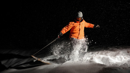 Active male snowboarder in orange sportswear and mask jumping on a snowy hill at night