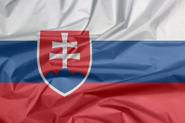 Fototapeta premium Fabric flag of Slovakia. Crease of Slovak flag background, white blue and red; charged with a shield containing a white cross is placed to left of center.