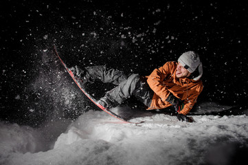 Happy snowboarder in orange jacket with stuck out tongue riding on a snowy hill at night