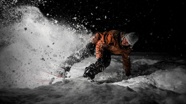 Smiling snowboarder in orange jacket riding on a snowy hill at night