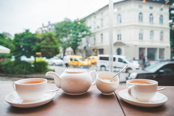 two cups with tea and white kettle in cafe table with big glass window