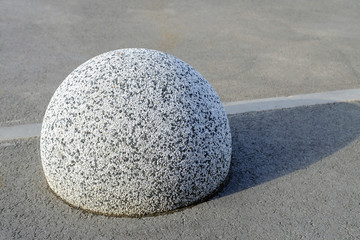 Fototapeta na wymiar Stone hemisphere on the asphalt in the Parking lot of granite chips