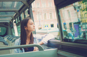 The girl rides a tourist bus and looks out the window.