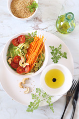 Vegetarian cuisine: raw zucchini and carrot spaghetti salad with cherry tomatoes, olives, cashew and olive oil, sesame dressing
