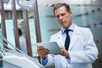 Modern technologies makes work easier. Dentist using his touchpad while standing in dentist’s office