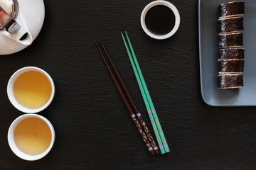 Japanese sushi with soy sauce on gray plate with chopsticks and traditional tea. Top view, close up on black concrete stone background
