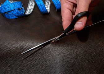 Tailor's hand cutting out leather with scissors, close up