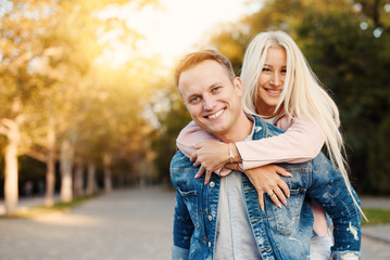 Fototapeta premium Closeup shot of young man carrying young woman on his back. Happy smiling couple looking at camera. Happy couple putdoor having fun piggyback in love.