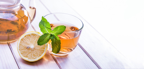 cup of tea, glass teapot, mint and lemon on wooden table