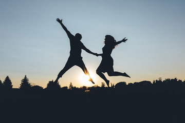 Couple bounces holding hands on the sunset, silhouette frame