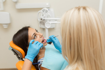 Pretty girl having mouth checkup in hospital by professional female dentist