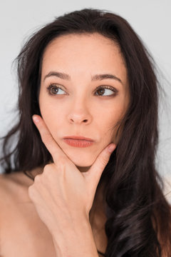 Caucasian girl with long dark hair without clothes on a white background. The girl in thoughts. Emotional shot.