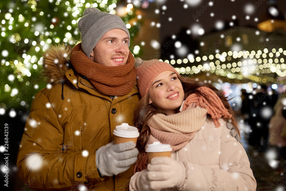 Wall mural winter holidays, hot drinks and people concept - happy young couple with coffee at christmas market in evening