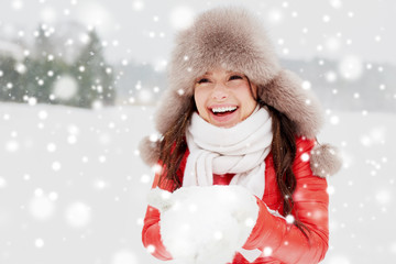 people, season and leisure concept - happy woman in winter fur hat holding snow in her hands outdoors