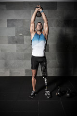 Athletic man with prosthesis lifting kettlebell