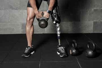 Crop man with prosthesis lifting kettlebell
