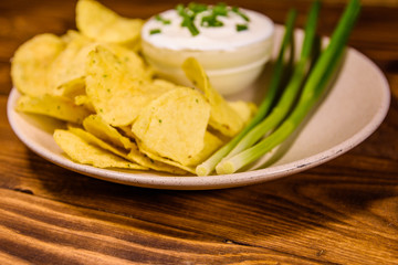 Ceramic plate with potato chips and glass bowl with sour cream on wooden table