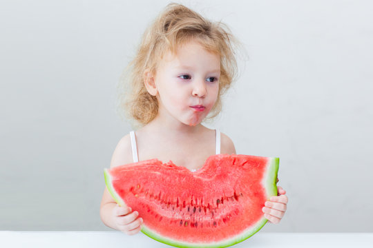 cute little baby girl eating watermelon slice on light background