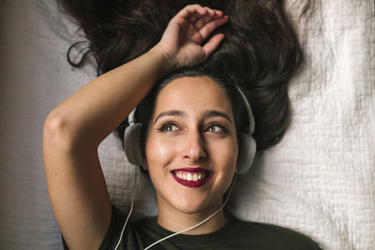 Overhead view of smiling teenage girl listening music on headphones while lying at home