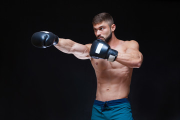 Strong muscular boxer in black boxing gloves. Isolated on black background.