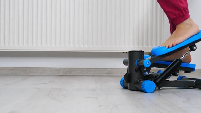 Woman doing exercises at home on stepping machine. Female legs foot on stepper trainer