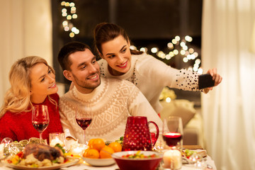 holidays and celebration concept - happy friends taking selfie by smartphone at home christmas dinner