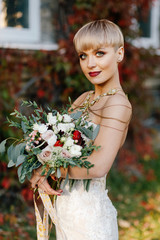 portrait of a stylish bride with short hair on a background of a wall made of autumn leaves