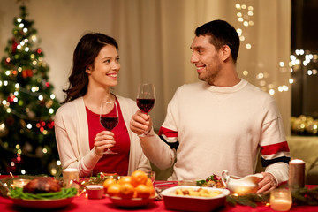holidays, family and celebration concept - happy couple having christmas dinner at home and drinking red wine