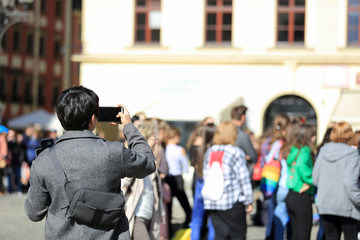 Mężczyzna z plecakiem robi zdjęcia telefonem komurkowym, smartfonem we Wrocławiu. - obrazy, fototapety, plakaty