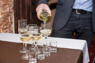 Man's hand pours champagne, white wine from bottle in wineglasses on table