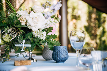 Festive round table with a blue tablecloth, dishes, wine glasses and a bouquet of flowers in the center