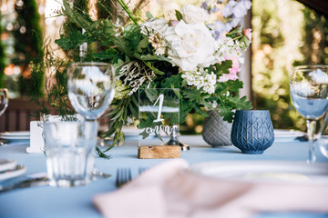 Festive round table with a blue tablecloth, dishes, wine glasses and a bouquet of flowers in the center
