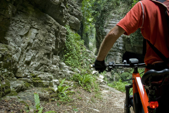 man with an electric bike, e-bike, ebike, mtb, mountain, rock canyon created by a river, forest, summer, sport, adventure, freedom, alps, Path called "Strada della Forra", Garda Lake, Lombardy, Italy