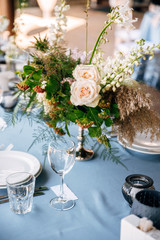 Festive table decorated with flowers and candles on a silver candlestick on blue tablecloth