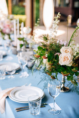 Festive table decorated with flowers and candles on a silver candlestick on blue tablecloth