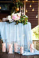 Festive table with long skyblue tablecloth decorated with candles in rustic candlesticks, peach color flowers on table