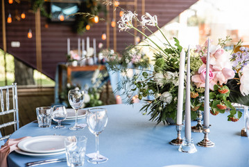 Long festive table with blue tablecloth decorated with flowers and candles